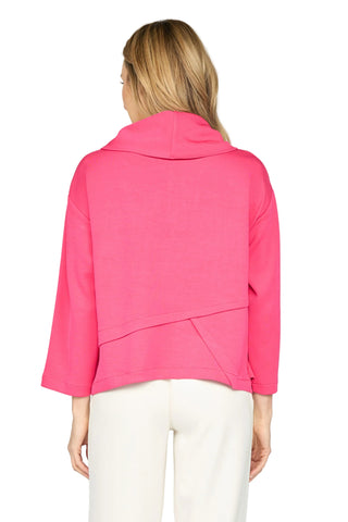 A woman viewed from the back wearing a bright pink cropped hoodie with long sleeves and draped seam details, paired with off-white pants, against a light gray studio background.