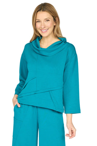 A woman modeling a matching teal cowl-neck long-sleeve top and wide-leg trousers set against a light gray studio background.
