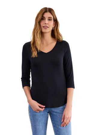 Woman wearing a black long-sleeve top and blue jeans against a light gray background