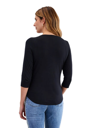 Woman wearing a black long-sleeve top and blue jeans on a light gray background