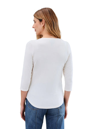 Woman wearing a white long-sleeve top and blue jeans against a plain background