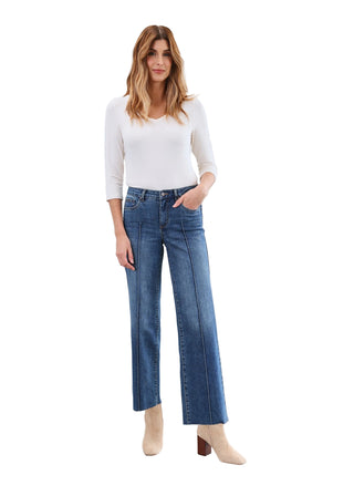 Woman wearing a white top and blue jeans against a plain background