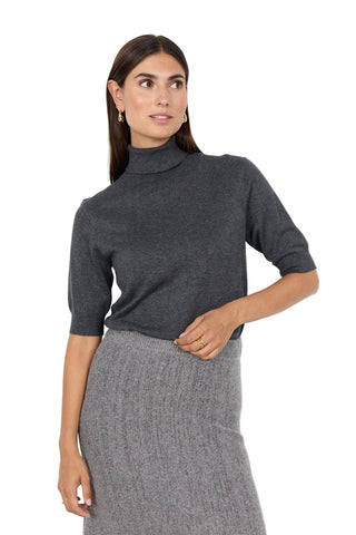 Woman wearing a gray turtleneck sweater and gray skirt against a white background