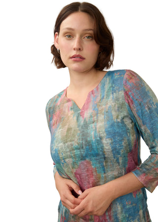 A woman wearing a three-quarter sleeve V-neck dress with an abstract watercolor print in shades of blue, pink, and beige, photographed against a neutral light gray background.