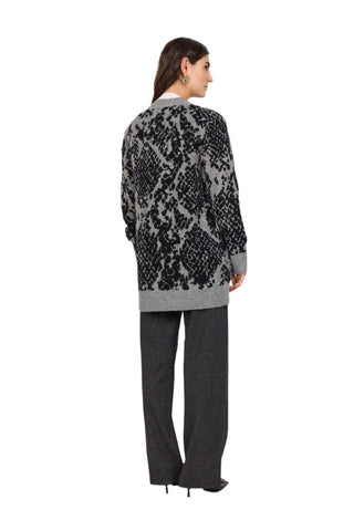 Person wearing a patterned cardigan and gray pants against a white background