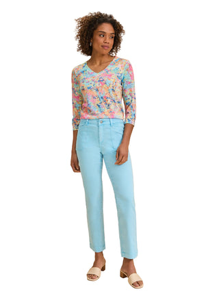 Woman wearing a colorful floral top and light blue jeans on a beige background