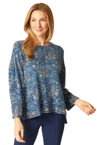 Woman wearing a blue patterned top and dark pants on a white background