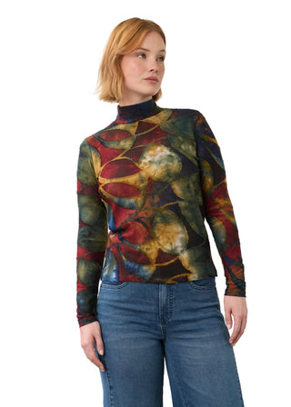 A woman wearing a long-sleeve mock neck top with an abstract multicolor print in red, green, yellow, and blue, paired with blue jeans, photographed against a plain light gray background.