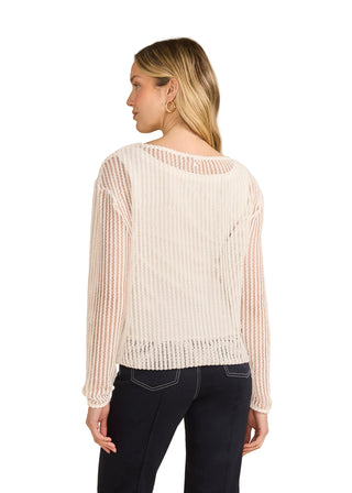 Woman wearing a white textured sweater and dark jeans on a beige background