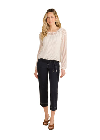 Woman wearing a white ribbed sweater and dark jeans on a beige background