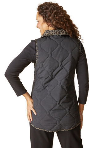 Person wearing a black quilted vest with a beige background