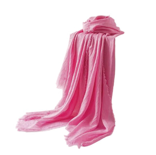 Pink scarf draped over a white box with a vase and branch on a light background