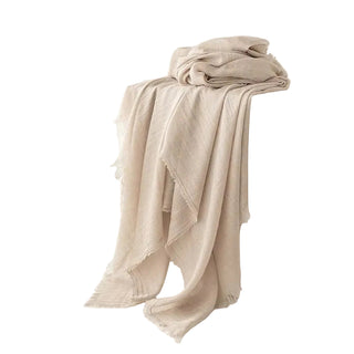 Beige blanket draped over a white cube with a vase and green branches on a light background