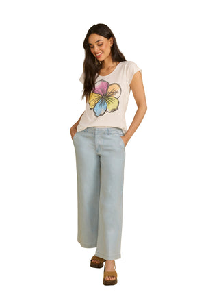 Woman wearing a white t-shirt with a colorful flower design and light blue jeans on a beige background