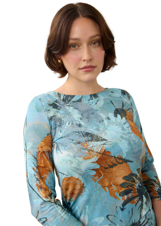 A woman with a short brown bob hairstyle wearing a light blue long-sleeve top with an abstract floral print in brown, orange, and gray, set against a plain light gray background.