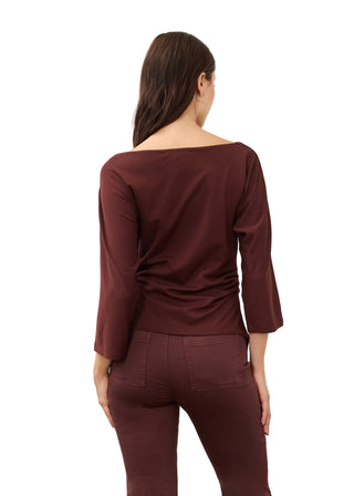 A woman viewed from the back wearing a wide-neck, three-quarter sleeve burgundy top and matching burgundy pants against a plain light gray studio background.