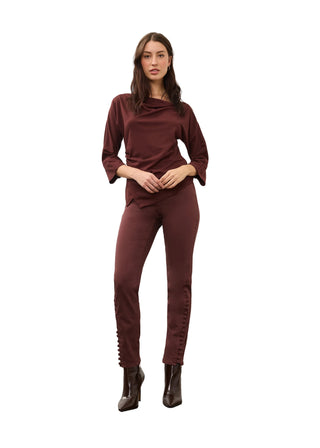 A woman modeling a matching two-piece outfit consisting of a long-sleeve cowl-neck top and slim-fit pants in a deep burgundy color, paired with dark brown ankle boots, against a plain studio background.