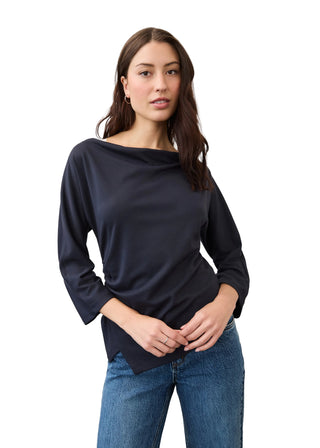 A woman modeling a dark navy blue boat-neck top with three-quarter sleeves, paired with blue jeans, against a neutral studio background.