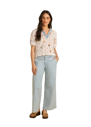Woman wearing a floral blouse and light blue jeans against a beige background