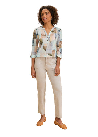 Woman wearing a patterned blouse and beige pants on a beige background