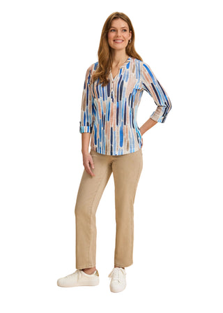 Woman wearing a patterned blouse and beige pants on a beige background