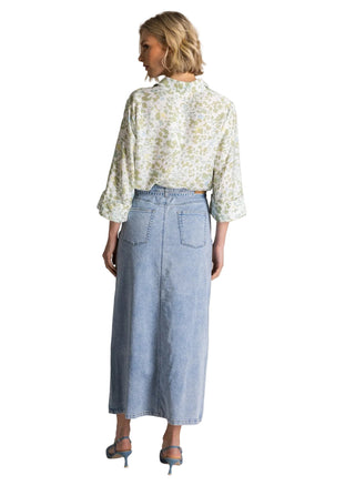 Woman wearing a floral blouse and denim skirt on a plain background