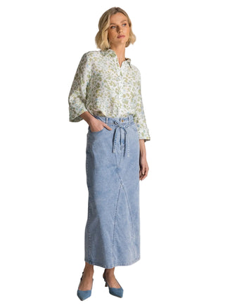 Woman wearing a floral blouse and denim skirt against a plain background