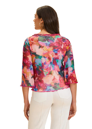 Woman wearing a colorful floral blouse with white pants on a beige background
