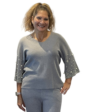 Woman wearing a gray outfit with embellished sleeves against a white background