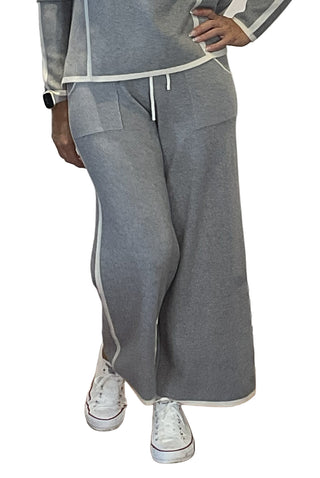 Person wearing a gray tracksuit with white sneakers in front of a white wall with text.