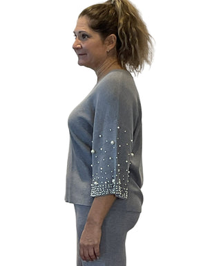 Woman wearing a gray sweater with pearl embellishments on sleeves against a white background