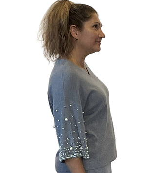 Woman wearing a gray outfit with pearl embellishments on sleeves against a white background