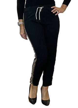 Person wearing black jogger pants with white drawstring and side stripe, standing against a white wall with branding.