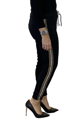 Person wearing black pants with a white stripe, high heels, and a watch on a plain background.