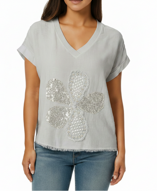 Woman wearing a light gray t-shirt with a decorative silver flower design on a white background