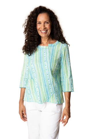 Woman wearing a light blue and green striped blouse with white pants against a beige background