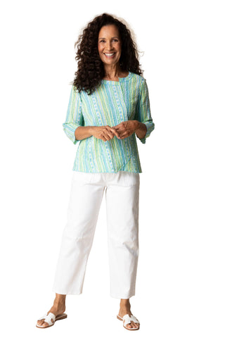 Woman wearing a striped shirt and white pants against a beige background