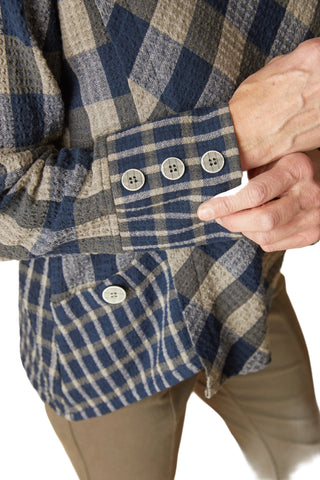 Close-up of a person wearing a blue, gray, and beige plaid flannel shirt, showing the buttoned cuffs and front pocket.