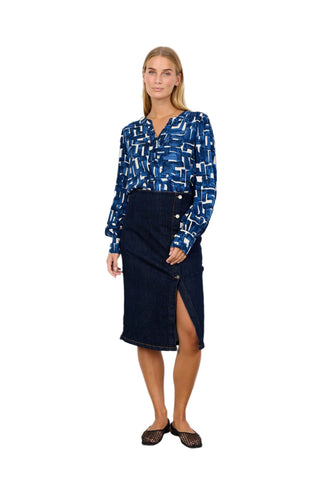 Woman wearing a blue patterned blouse and navy skirt against a white background