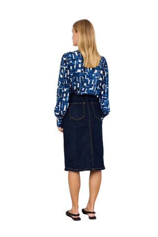 Woman wearing a blue patterned blouse and dark denim skirt against a white background