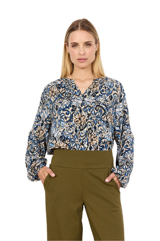 Woman wearing a patterned blouse and green pants against a white background