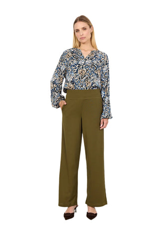 Woman wearing a patterned blouse and olive green pants against a white background