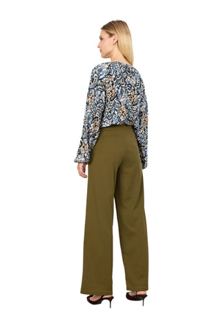 Woman wearing a patterned blouse and olive green pants against a white background