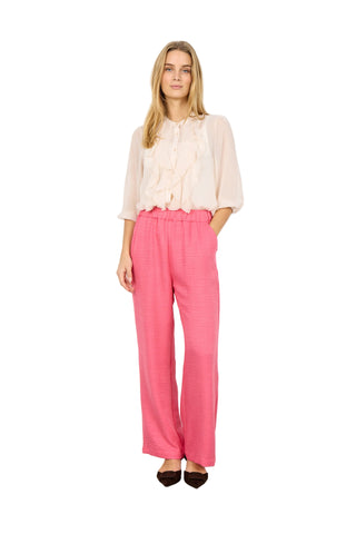 Woman wearing a white blouse and pink pants against a white background