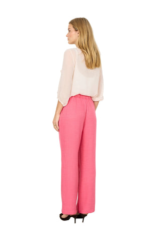 Woman wearing a light pink blouse and bright pink pants against a white background