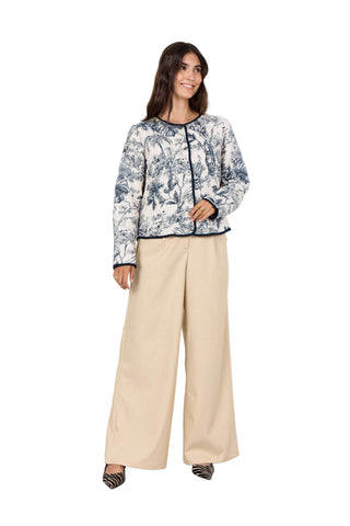 Woman wearing a patterned top and beige pants against a white background