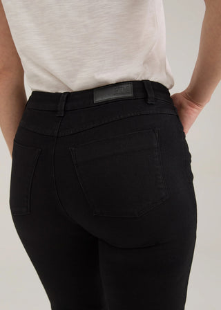 Close-up back view of a person wearing black high-waisted skinny jeans with a white top, showing the back pockets and waistband.