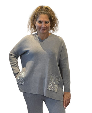 Woman wearing a gray sweater with sequin pockets against a white background