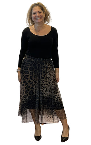 Woman wearing a black top and leopard print skirt against a white wall with 'The Avenue' branding.