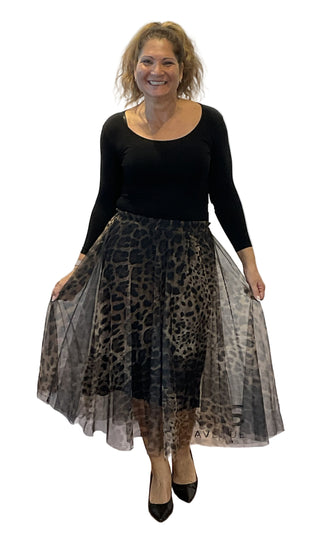 Woman wearing a black top and leopard print skirt against a white wall.